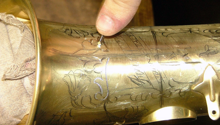 Hands engraving a saxophone bell in an Italian workshop
